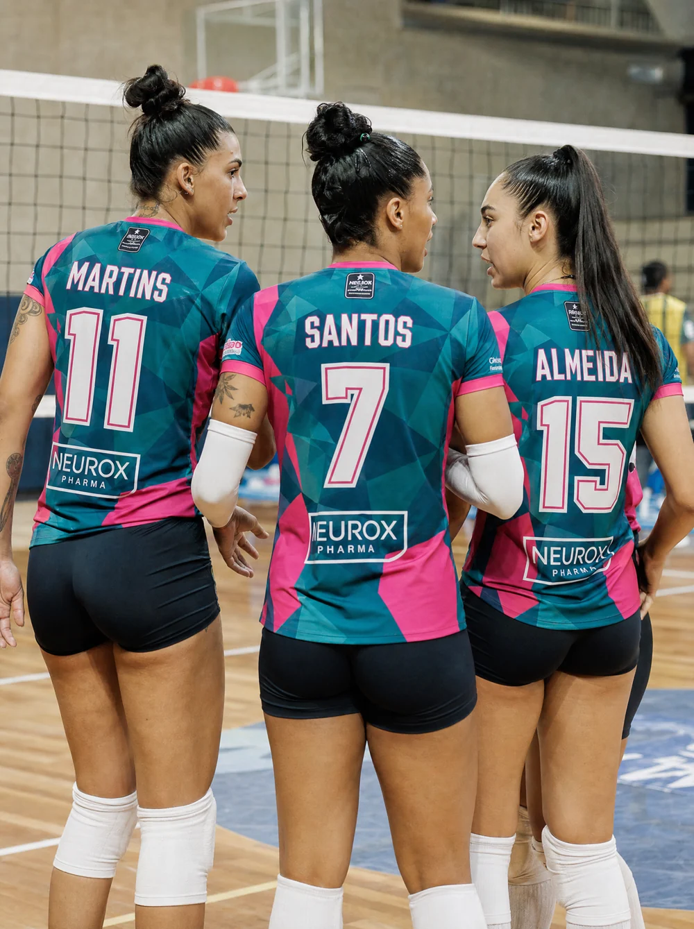 Trio feminino de vôlei de quadra de costas mostrando números e nomes nas costas com logos de patrocinadores